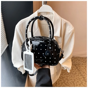 Close-up of black patent leather bowling bag with white heart pattern and luggage tag detail