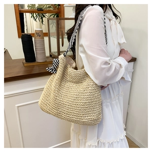 Dettaglio della borsa tote in paglia intrecciata beige con tracolla a righe su modella