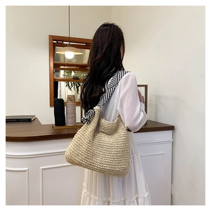 Dettaglio della borsa tote in paglia intrecciata con tracolla in tessuto a righe e frange