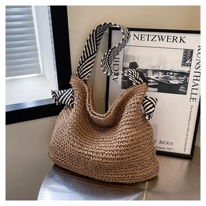 Dettaglio della borsa tote in paglia con tracolla a righe bianche e nere e fiocco decorativo