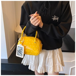 Detail of a bright yellow boston bag featuring white heart prints and stylish tag accessory