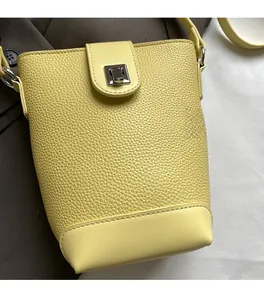 Close-up of bright yellow bucket bag featuring pebble leather texture and silver turn-lock