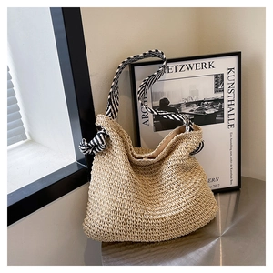 Dettaglio della borsa tote in paglia beige con manico decorativo in sciarpa a righe bianche e nere