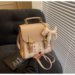 Detail showing beige teddy bear crossbody bag with puppy charm and golden hardware buckle