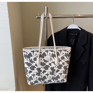 Close-up of cow print tote bag with leather trim and embossed logo on metal hanger
