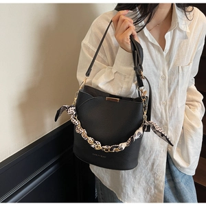 Detail view of black lychee-textured bucket bag with polka dot scarf on golden chain