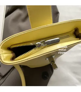 Detailed close-up of the smooth silver zipper and metal buckle on yellow leather bucket bag