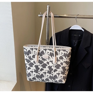 Detail of a cow print tote bag with MEIGEBAG logo hanging against a black blazer