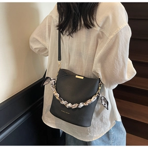 Detail of black pebbled leather bucket bag with decorative polka dot scarf and gold logo