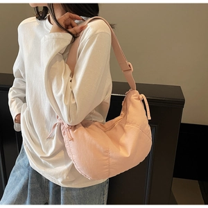 Side view of pink dumpling shoulder bag with adjustable strap worn by model
