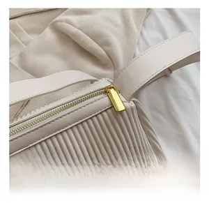 Close-up of golden zipper hardware and pleated texture on a cream crossbody bag