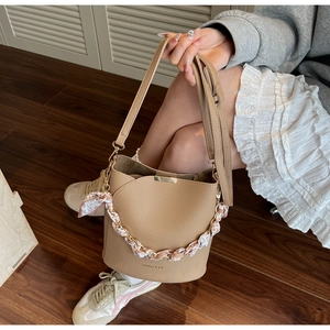 Detail of beige bucket bag with silk scarf wrapped chain handle and textured leather finish