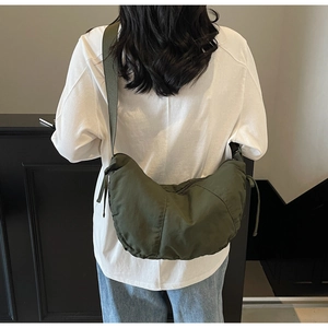 Detail of dark green crescent hobo bag with stitched seams worn by a model in casual style