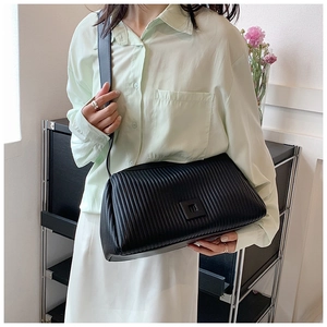 Close-up of black quilted shoulder bag with vertical pleats and square buckle on model