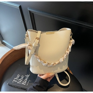 Close-up of beige bucket bag with lychee texture leather and chain silk scarf strap