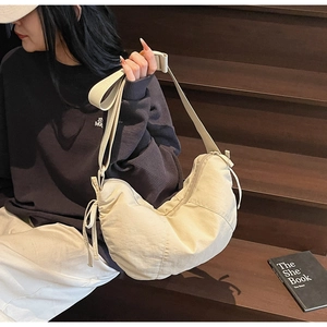Detail of beige crescent bag featuring drawstring bow decoration and adjustable strap
