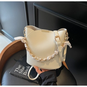 Detail of cream bucket bag featuring a printed silk scarf on gold chain and brand logo