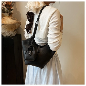 Detail of black pebbled leather bucket bag with matching mini pouch on casual shoulder model