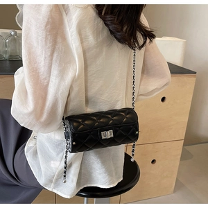 Detail of black quilted cylindrical crossbody bag with silver turn-lock and chain strap