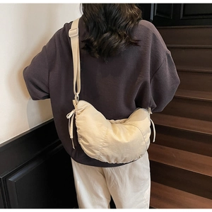 Beige crescent dumpling bag with drawstring details shown on a model's shoulder