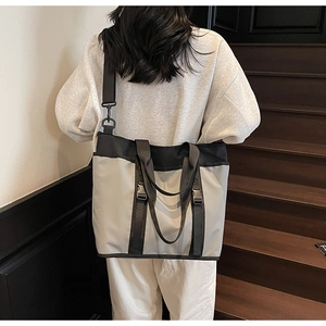 Close-up of a large grey and black tote bag with adjustable straps on a model