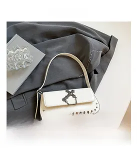 Close-up of white crossbody bag with metal cross charm, chain and rivet details