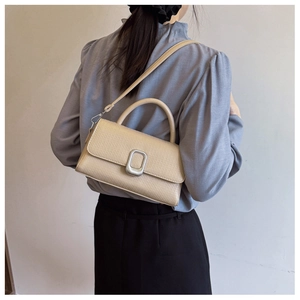 Detail of beige textured leather handbag featuring a rectangular silver buckle and top handle