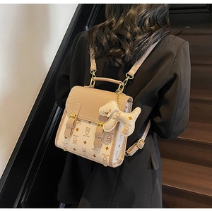 Detail view of beige bear-patterned backpack with golden clasp and plush dog charm