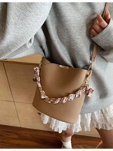 Minimalist camel bucket bag with scarf-wrapped chain strap and textured leather finish