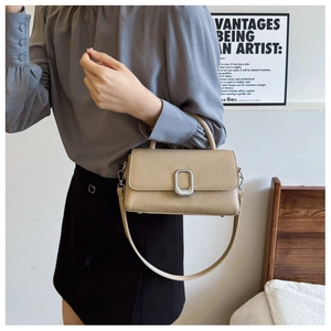 Detailed view of beige textured leather crossbody bag with silver buckle and top handle