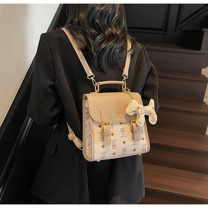 Detail of beige cartoon bear patterned backpack with golden hardware and plush charm