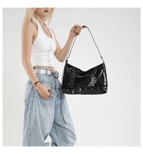 Close-up of black glossy leather crossbody bag with punk metal eyelets and chain details
