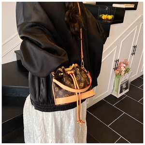 Detail of a brown bucket bag with monogram pattern and drawstring closure on a model