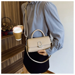 Detail of beige textured leather handbag with silver metal buckle and adjustable shoulder strap