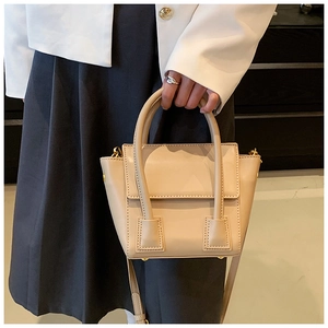 Close-up of beige trapezoid handbag with gold hardware and top handle on model