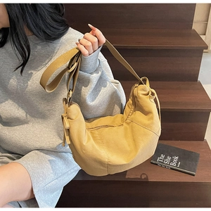 Close-up of khaki dumpling crossbody bag with wide woven strap on wooden steps