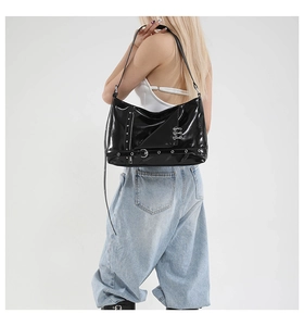 Side view of a black glossy punk-style shoulder bag with silver rings on a model