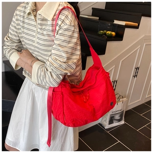 Close-up of bright red nylon dumpling bag with adjustable strap and logo detail