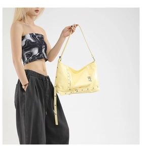 Close-up of yellow patent leather hobo bag with silver rivets and metal zipper detail