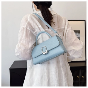 Detail of light blue textured leather crossbody bag with silver oval metal buckle