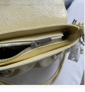 Détail des fermetures éclair argentées et de la texture plissée crème sur le sac