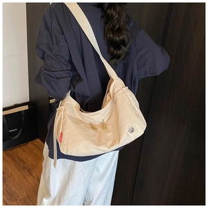 Detail of beige nylon crossbody bag featuring wide shoulder straps and side red label tag