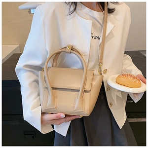 Detail of beige PU leather handbag showing round handles and gold hardware accents