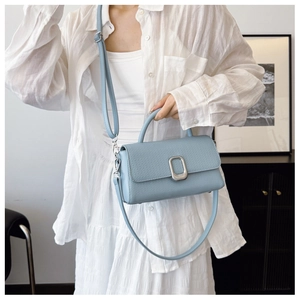 Detail of light blue textured leather crossbody bag with silver buckle worn by a model