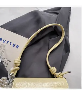 Détail du sac plissé crème avec poignée nouée et breloque élégante en perles blanches