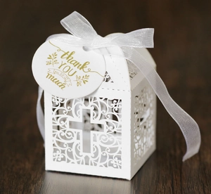 Close-up of laser-cut cross pattern on white candy box with ribbon and thank you tag