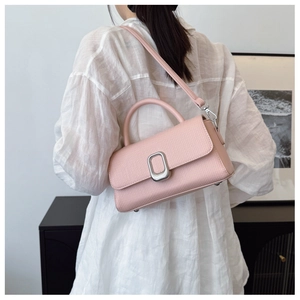 Detail of pink small leather crossbody bag with silver buckle worn on model over white shirt