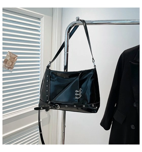 Detail of a shiny black punk style crossbody bag with metal rings and silver studs