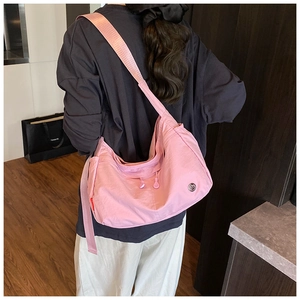 Pink nylon crossbody bag with wide strap and metallic logo shown on a female model