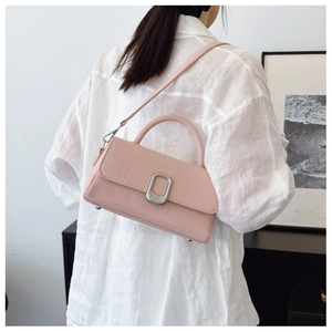 Detail of light pink crossbody bag with silver buckle and leather texture on a model